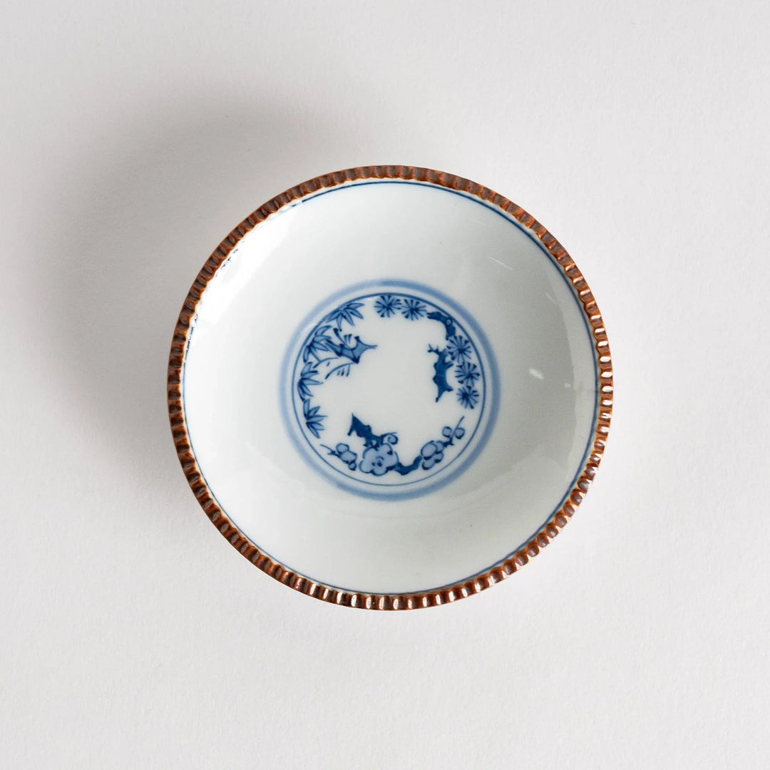 Small ceramic plate with central blue floral motif on white background framed by copper textured rim.