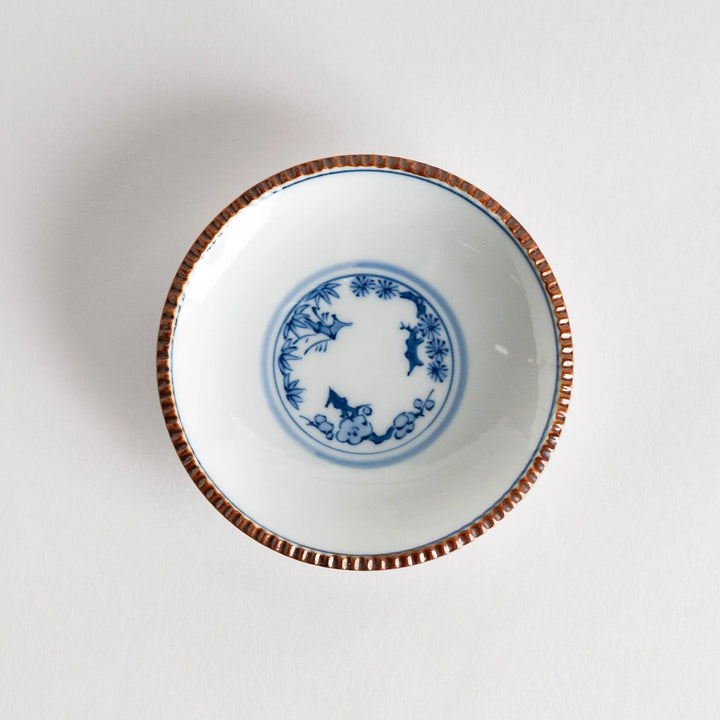 Small ceramic plate with central blue floral motif on white background framed by copper textured rim.