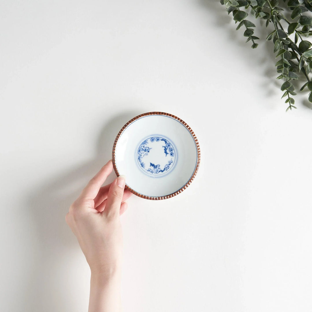 Small ceramic plate with central blue floral motif on white background framed by copper textured rim.