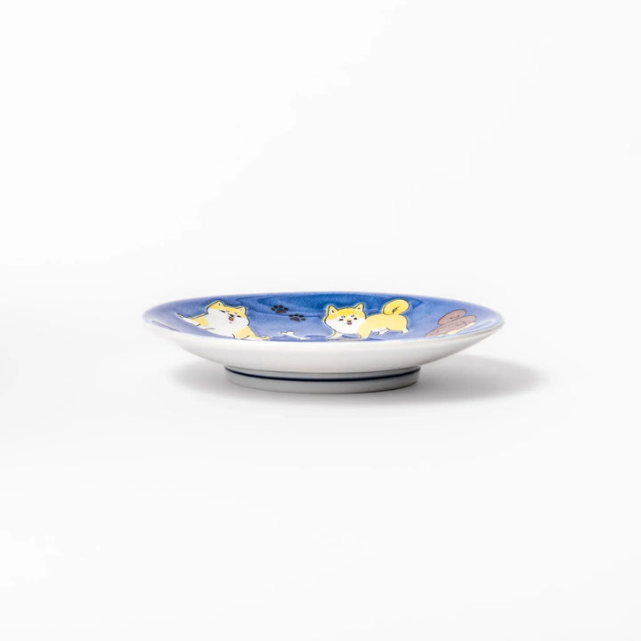Round Japanese ceramic sauce dish with deep blue background featuring playful Shiba Inu dogs and paw prints.