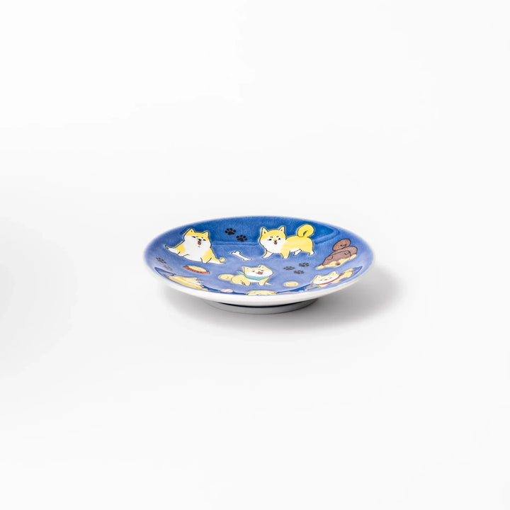 Round Japanese ceramic sauce dish with deep blue background featuring playful Shiba Inu dogs and paw prints.
