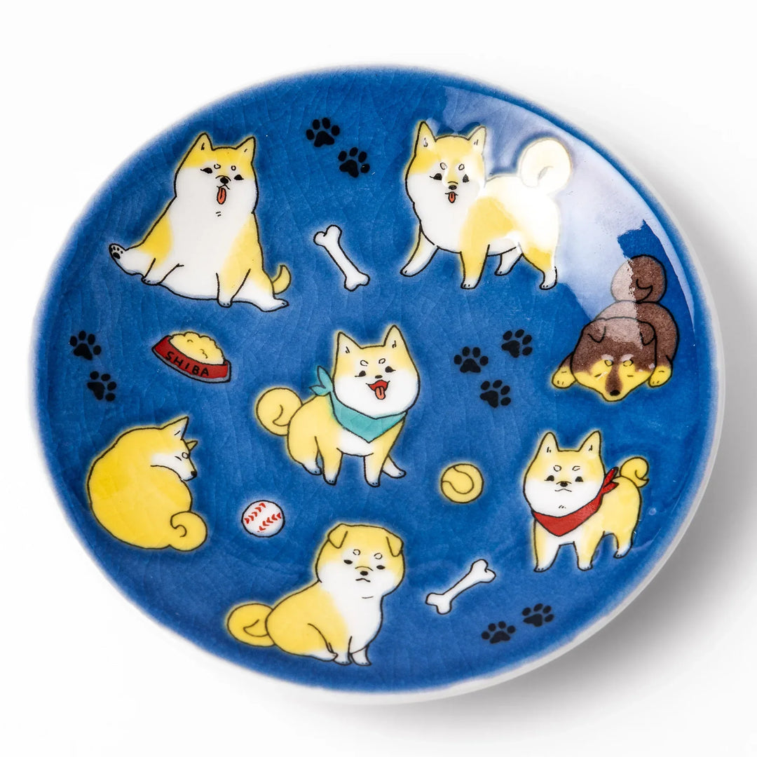 Round Japanese ceramic sauce dish with deep blue background featuring playful Shiba Inu dogs and paw prints.