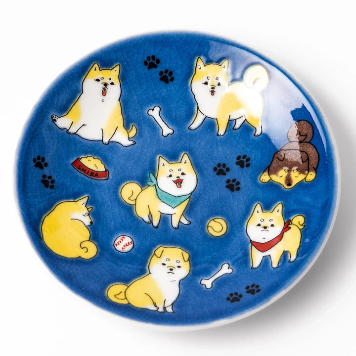 Round Japanese ceramic sauce dish with deep blue background featuring playful Shiba Inu dogs and paw prints.