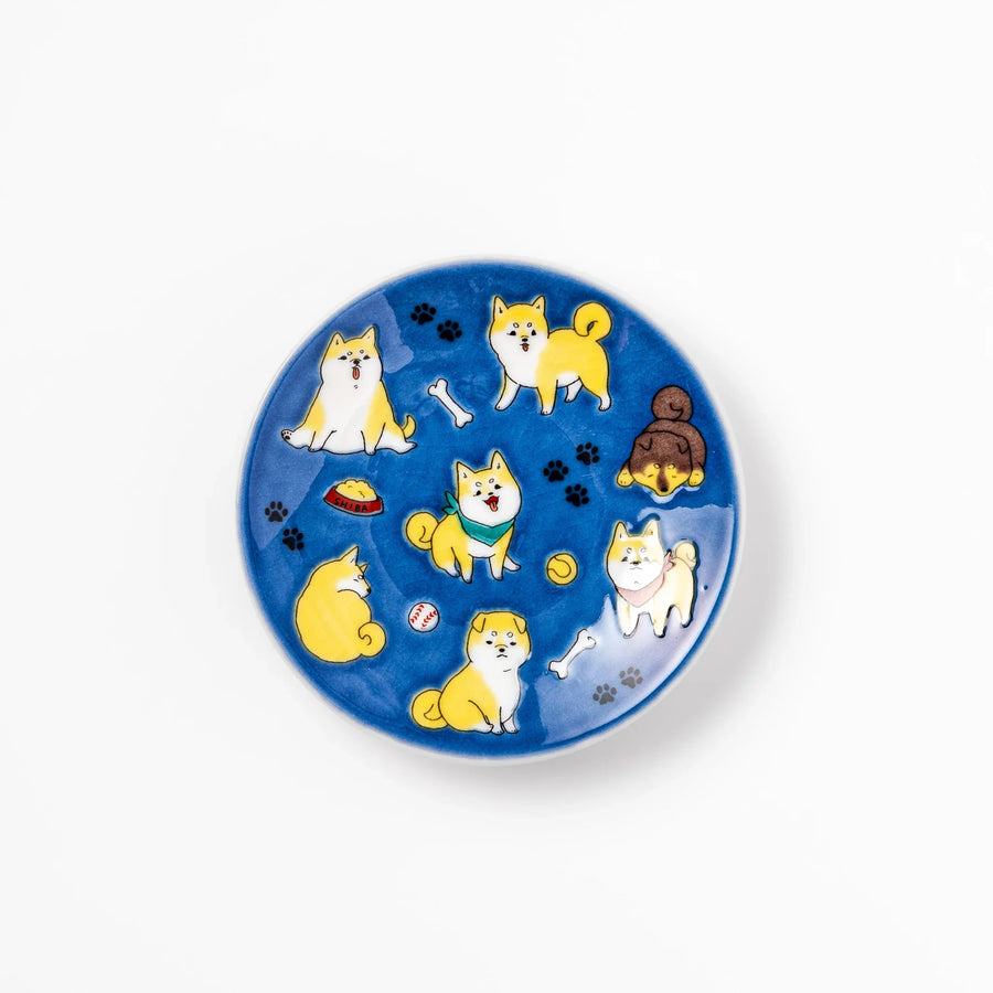 Round Japanese ceramic sauce dish with deep blue background featuring playful Shiba Inu dogs and paw prints.