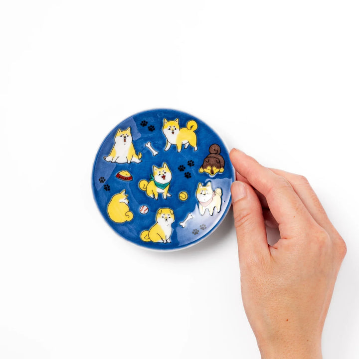 Round Japanese ceramic sauce dish with deep blue background featuring playful Shiba Inu dogs and paw prints.