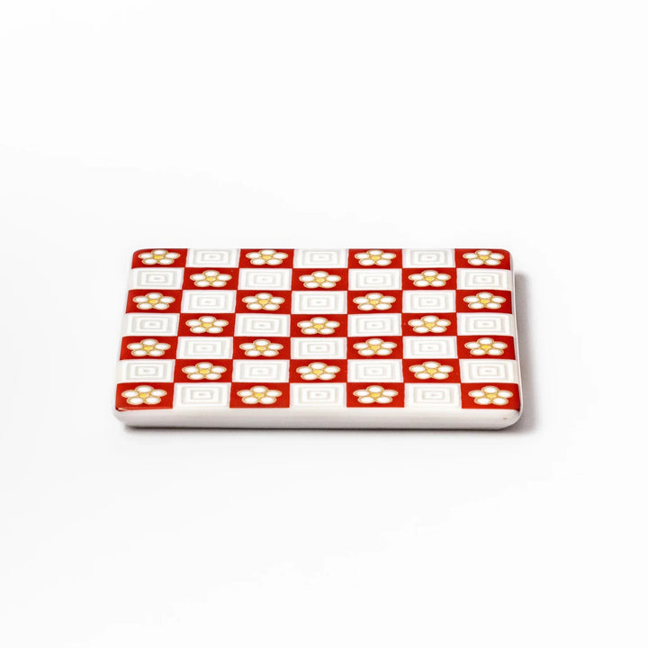 Square Japanese ceramic coaster with red and white checkered pattern and plum blossom motifs for dining.