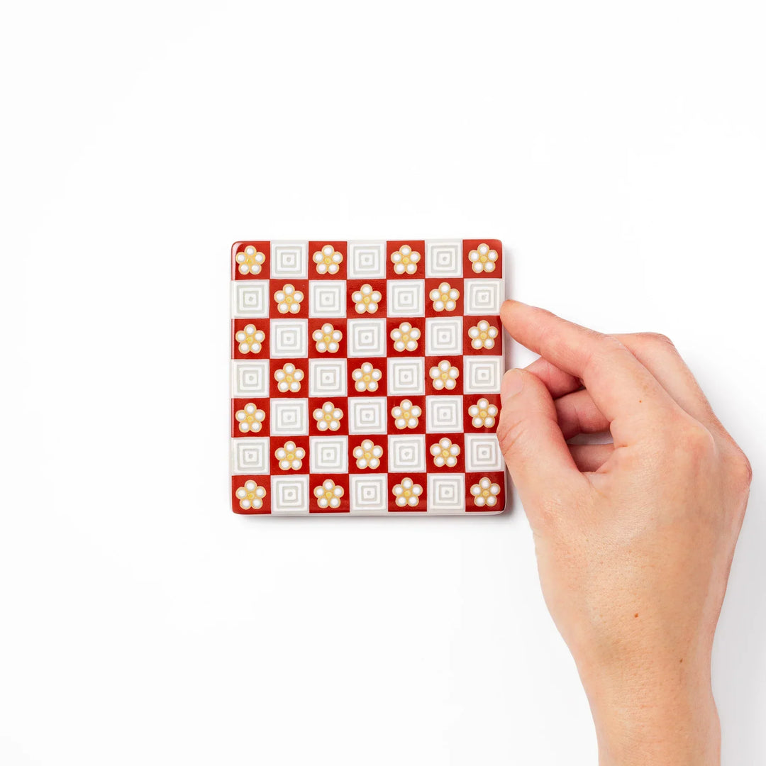 Square Japanese ceramic coaster with red and white checkered pattern and plum blossom motifs for dining.