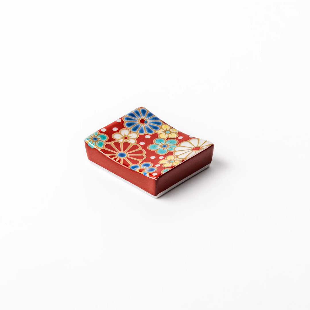 Rectangular Japanese ceramic chopstick rest with red background and plum and chrysanthemum designs.