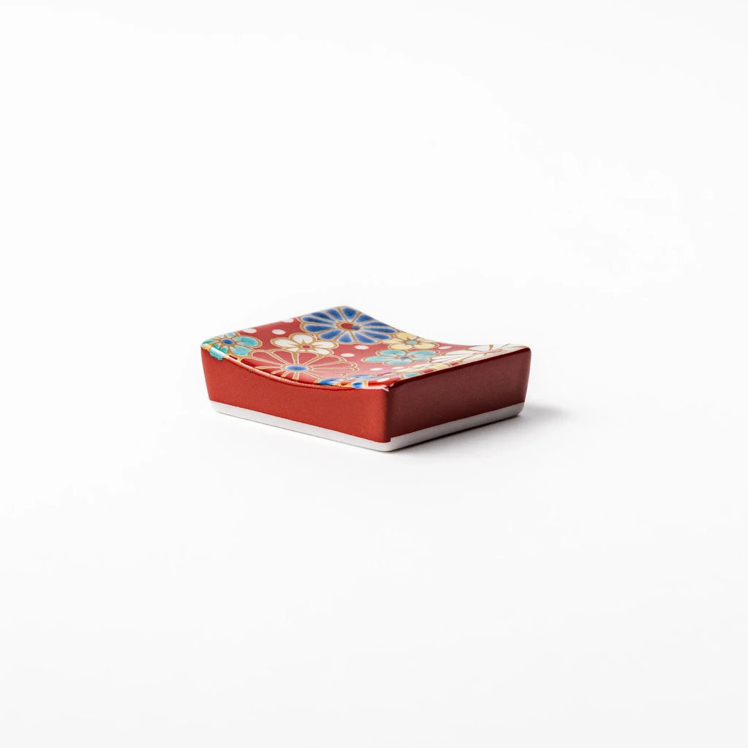 Rectangular Japanese ceramic chopstick rest with red background and plum and chrysanthemum designs.