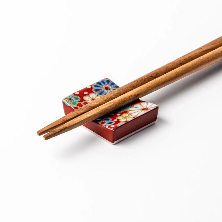 Rectangular Japanese ceramic chopstick rest with red background and plum and chrysanthemum designs.