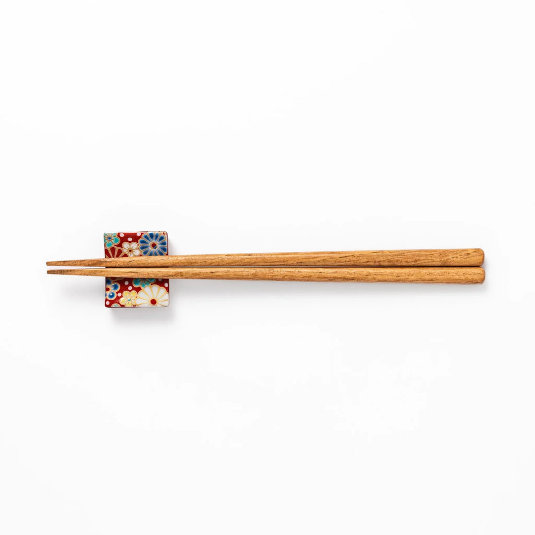 Rectangular Japanese ceramic chopstick rest with red background and plum and chrysanthemum designs.