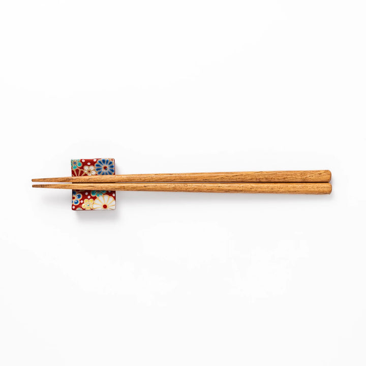 Rectangular Japanese ceramic chopstick rest with red background and plum and chrysanthemum designs.