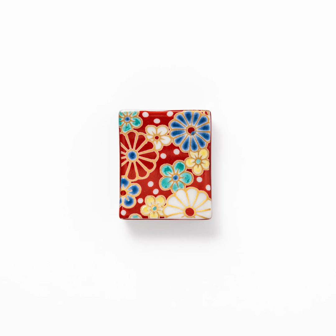 Rectangular Japanese ceramic chopstick rest with red background and plum and chrysanthemum designs.