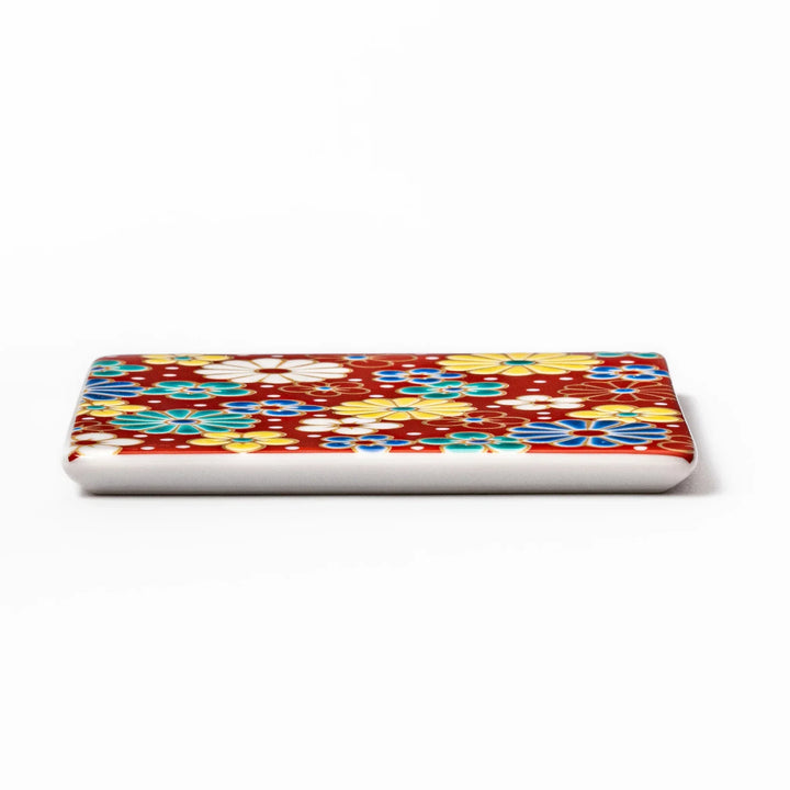 Square Japanese ceramic coaster with red background and plum and chrysanthemum designs for elegant tables.