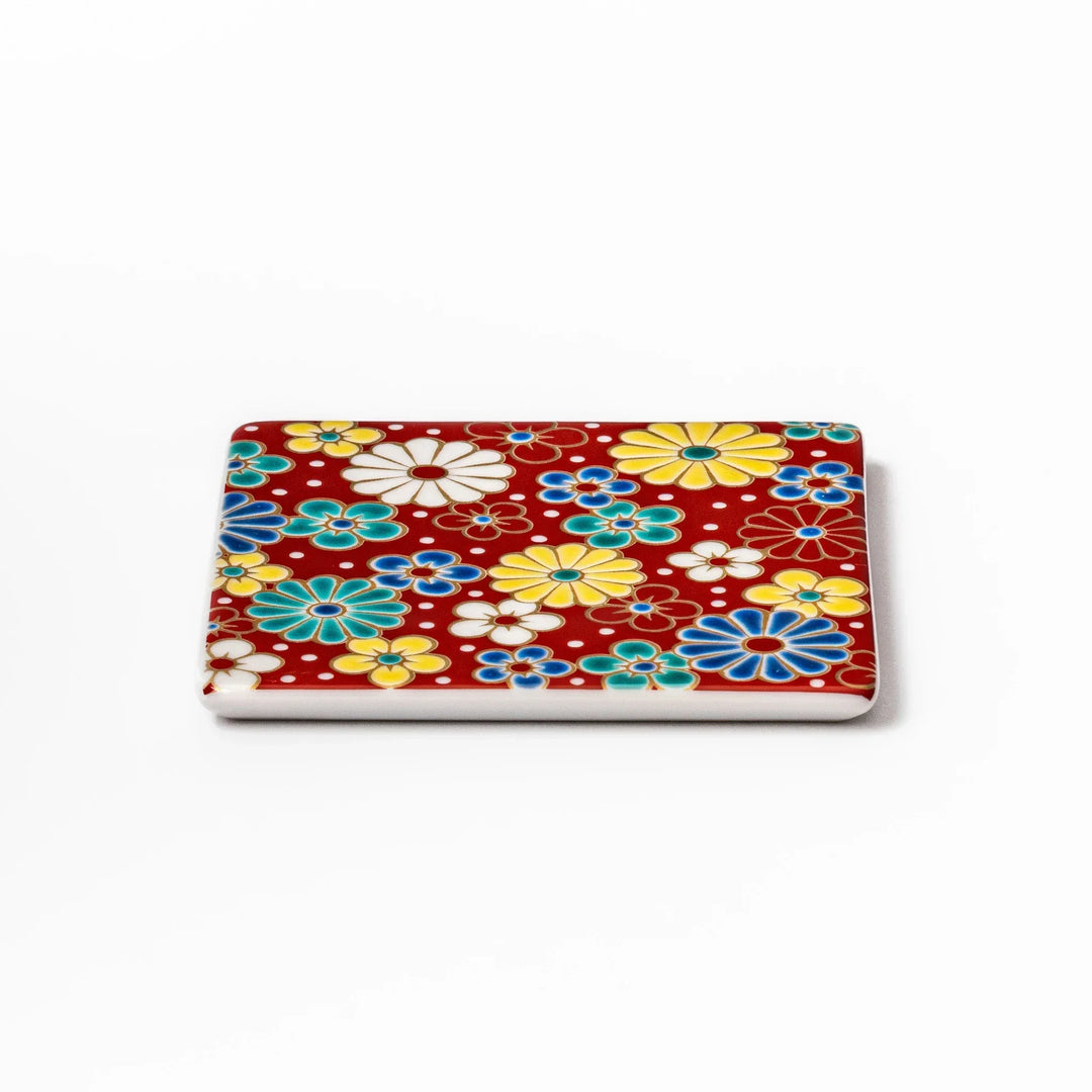 Square Japanese ceramic coaster with red background and plum and chrysanthemum designs for elegant tables.