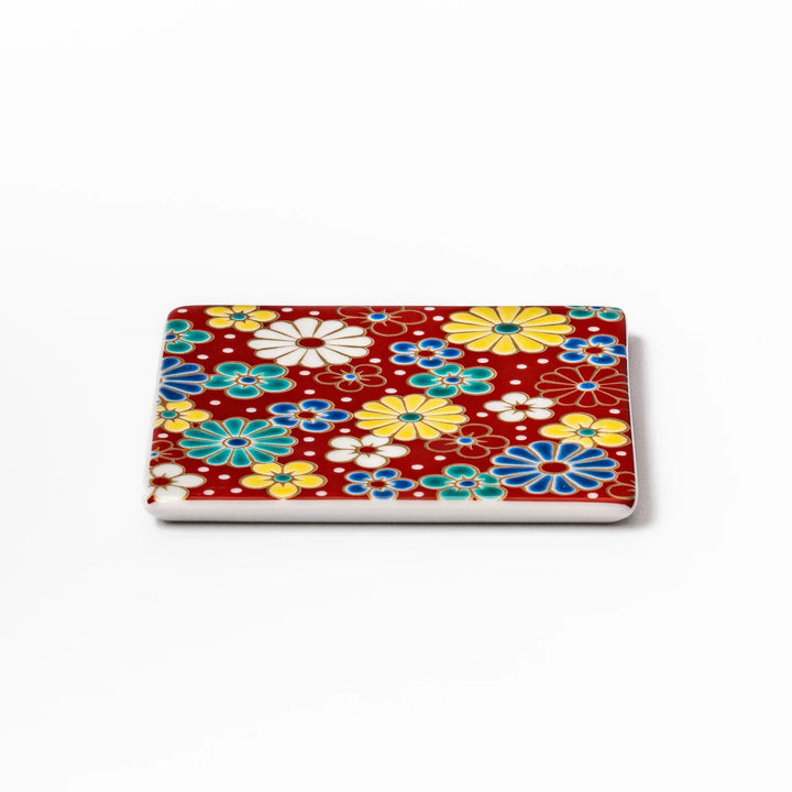 Square Japanese ceramic coaster with red background and plum and chrysanthemum designs for elegant tables.