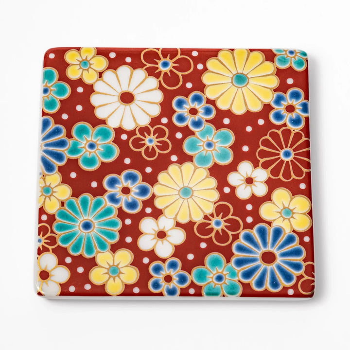 Square Japanese ceramic coaster with red background and plum and chrysanthemum designs for elegant tables.