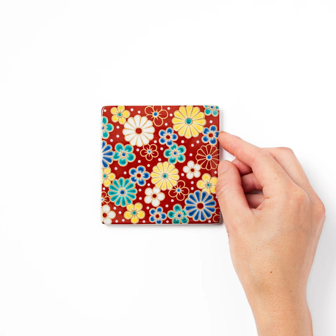 Square Japanese ceramic coaster with red background and plum and chrysanthemum designs for elegant tables.