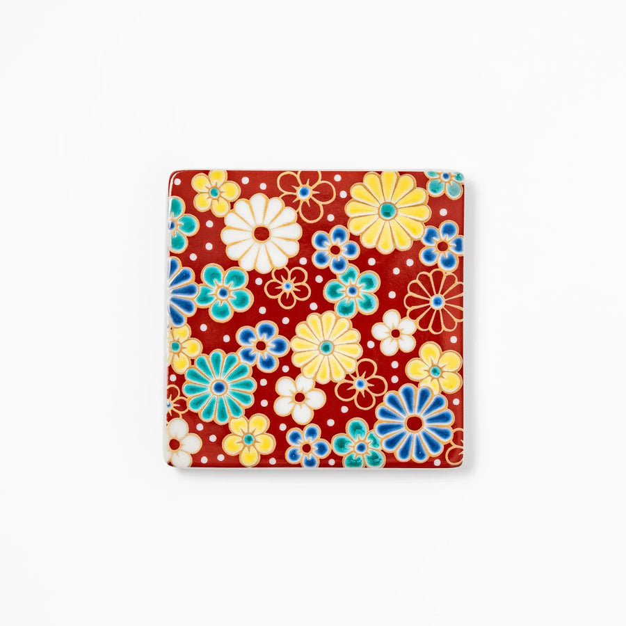 Square Japanese ceramic coaster with red background and plum and chrysanthemum designs for elegant tables.