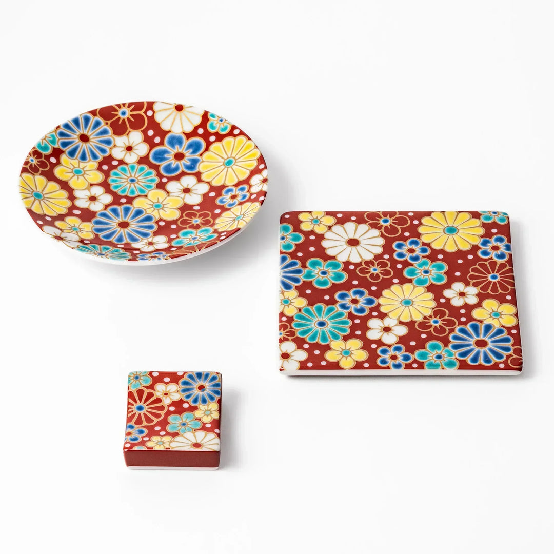 Japanese ceramic tableware set with red background plum and chrysanthemum motifs including dish and rest.