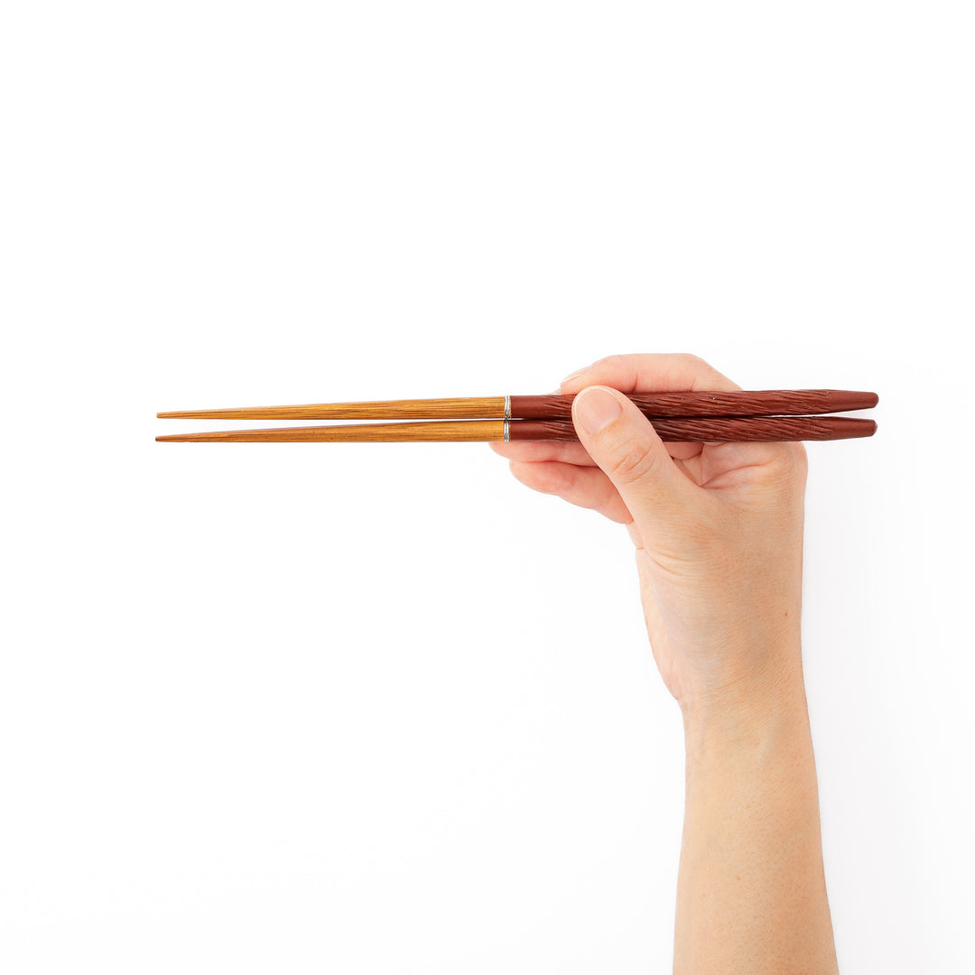 A hand holding red textured portable Japanese travel chopsticks showcasing a comfortable nonslip grip and standard length