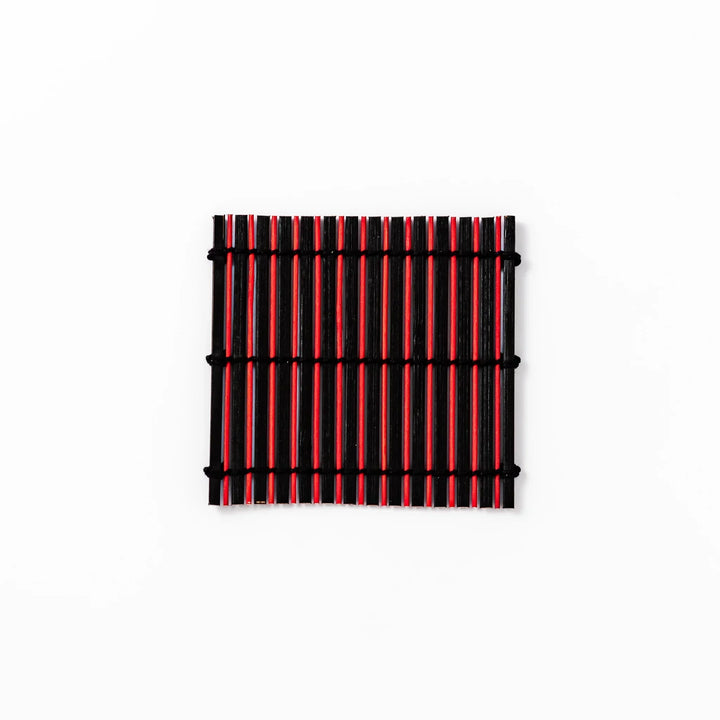 Red and black bamboo coaster with slim vertical slats and black cords for striking Japanese drink setting.