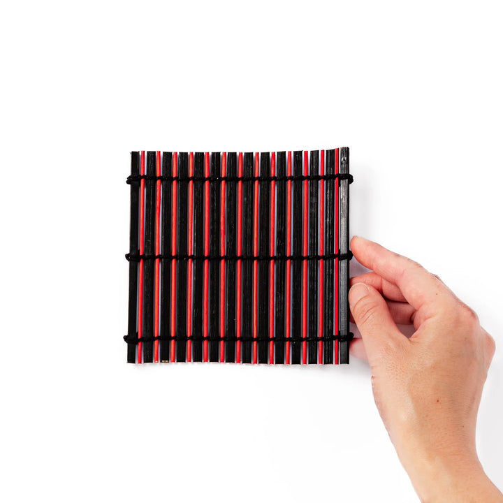 Red and black bamboo coaster with slim vertical slats and black cords for striking Japanese drink setting.