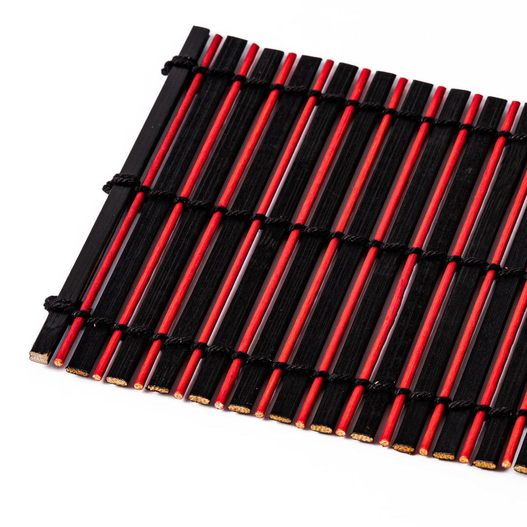 Red and black bamboo coaster with slim vertical slats and black cords for striking Japanese drink setting.