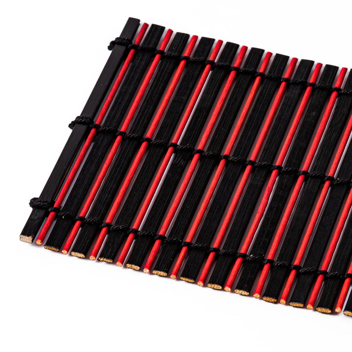 Red and black bamboo coaster with slim vertical slats and black cords for striking Japanese drink setting.