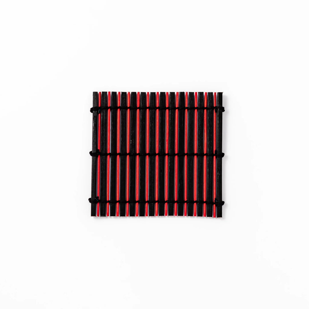 Red and black bamboo coaster with slim vertical slats and black cords for striking Japanese drink setting.