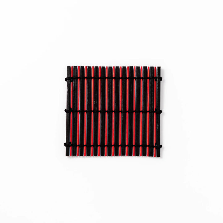 Red and black bamboo coaster with slim vertical slats and black cords for striking Japanese drink setting.