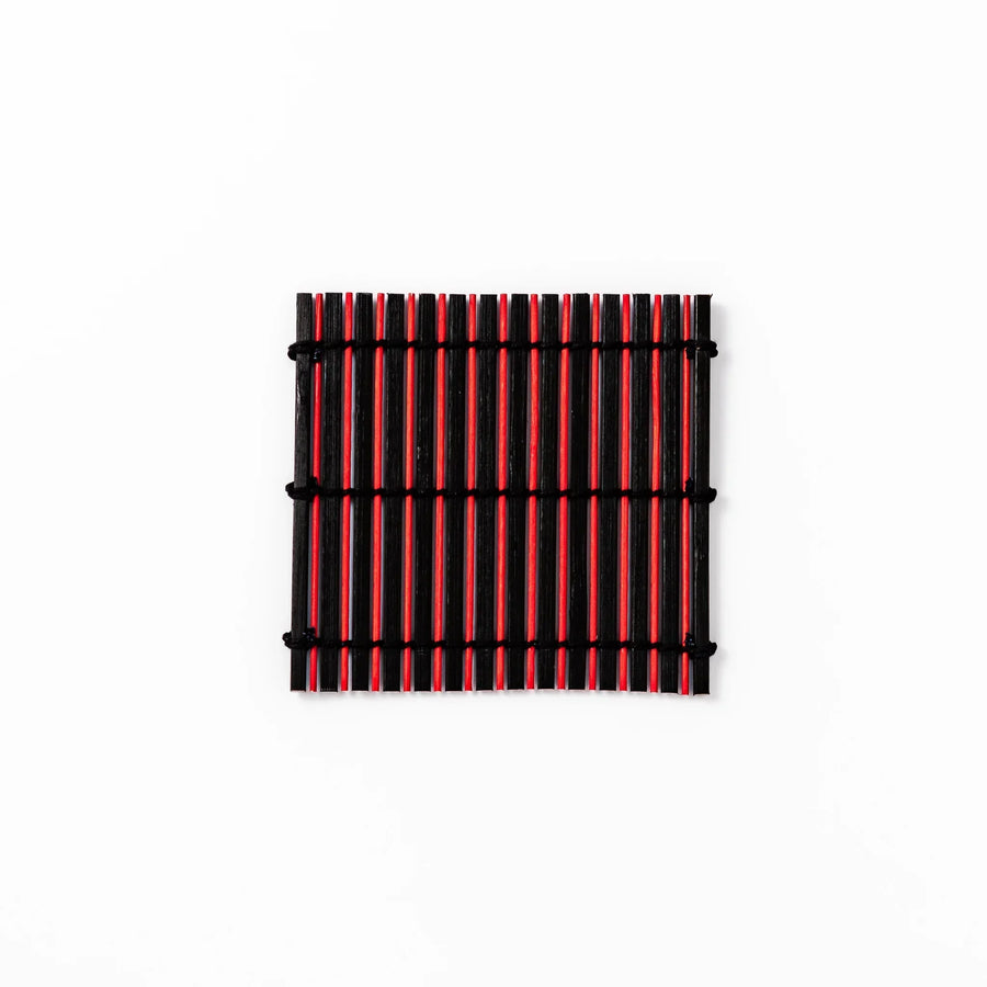 Red and black bamboo coaster with slim vertical slats and black cords for striking Japanese drink setting.
