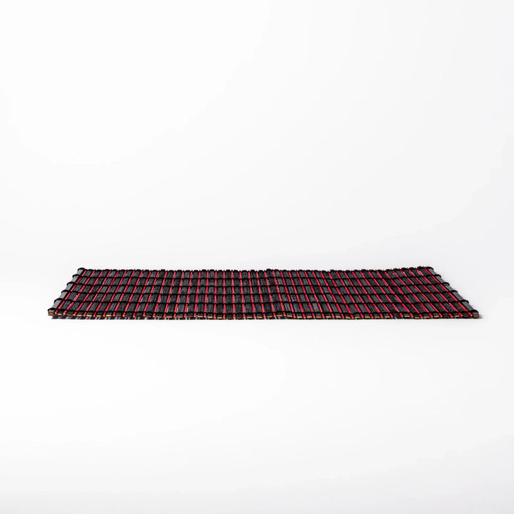 Red and black bamboo table mat with tight slats and black cords for bold modern Japanese table setting.