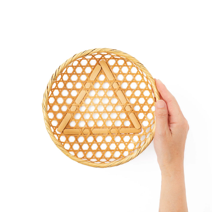 An open round handwoven bamboo serving basket with its hexagonal mesh pattern lid leaning slightly to the side