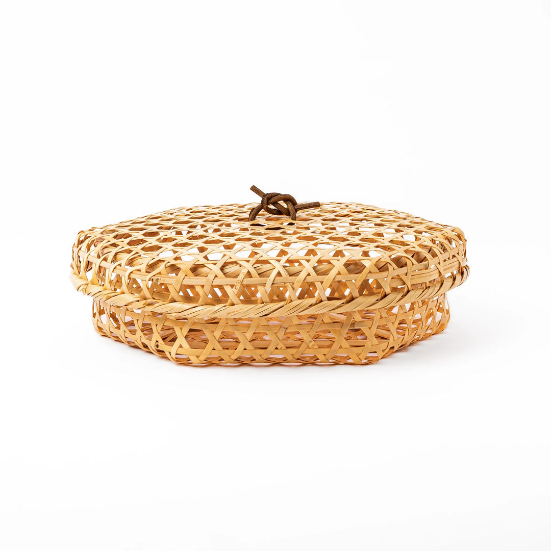 A medium round handwoven bamboo serving basket with a hexagonal mesh pattern lid resting on the woven border