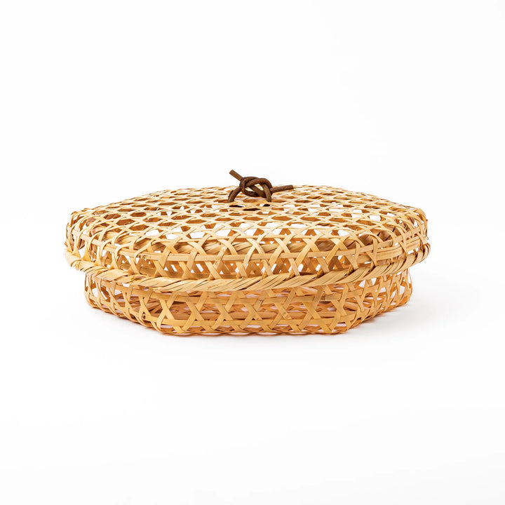 A medium round handwoven bamboo serving basket with a hexagonal mesh pattern lid resting on the woven border