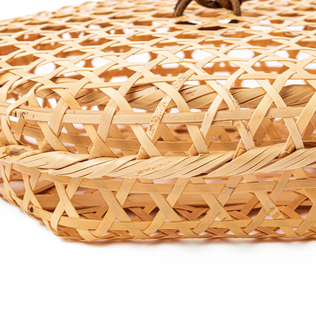 A medium round handwoven bamboo serving basket with a hexagonal mesh pattern lid resting on the woven border