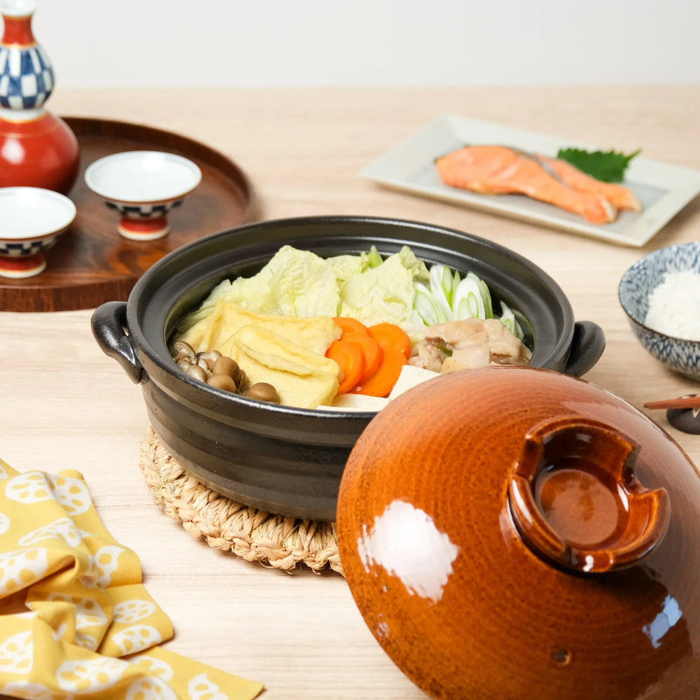 Japanese clay donabe with rustic glaze filled with vegetables, tofu, and mushrooms, set on a wooden table for a cozy meal.