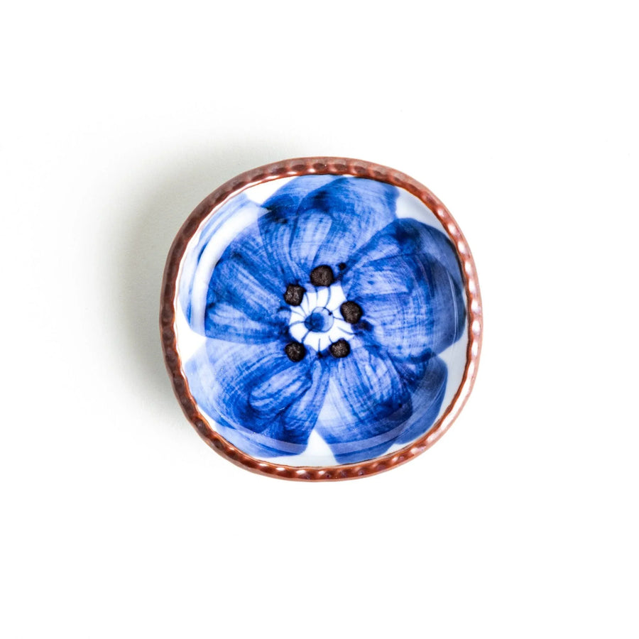A round plate featuring a large, bold blue flower with a textured brown rim.