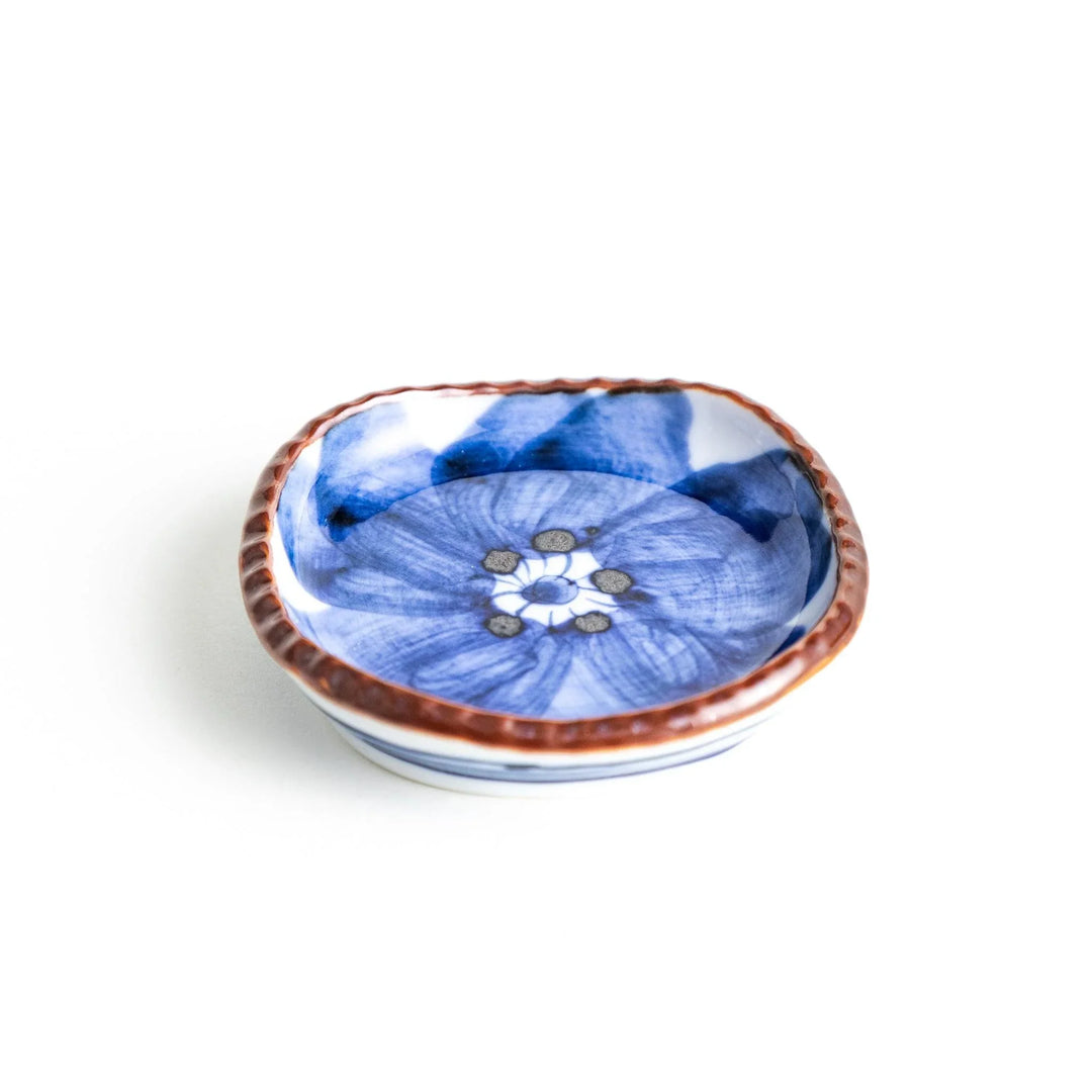 A round plate featuring a large, bold blue flower with a textured brown rim.