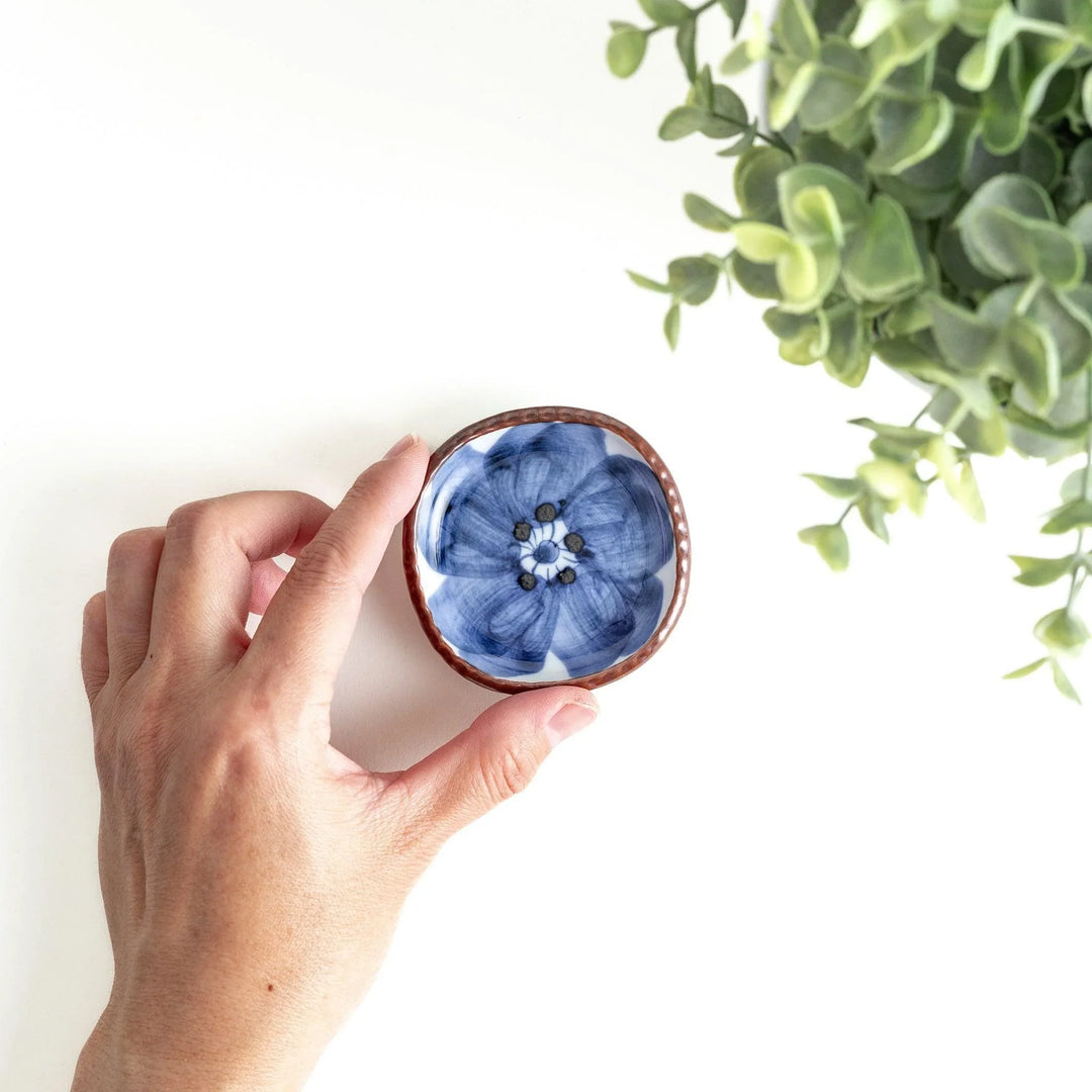 A round plate featuring a large, bold blue flower with a textured brown rim.