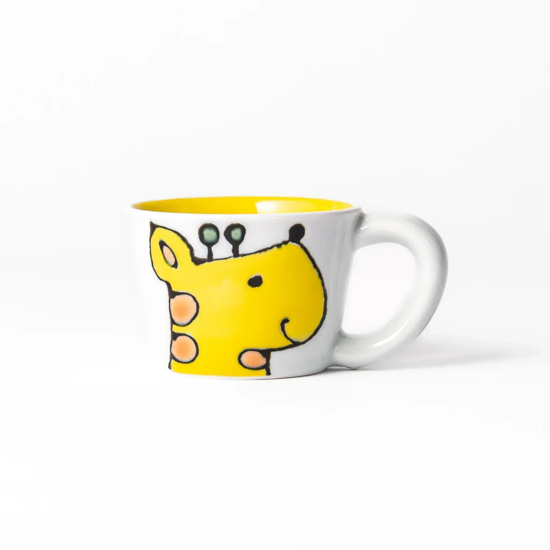 White ceramic kids’ mug with yellow giraffe and green ossicones, featuring a round handle and yellow interior.