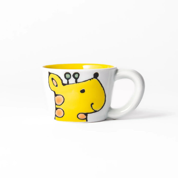 White ceramic kids’ mug with yellow giraffe and green ossicones, featuring a round handle and yellow interior.