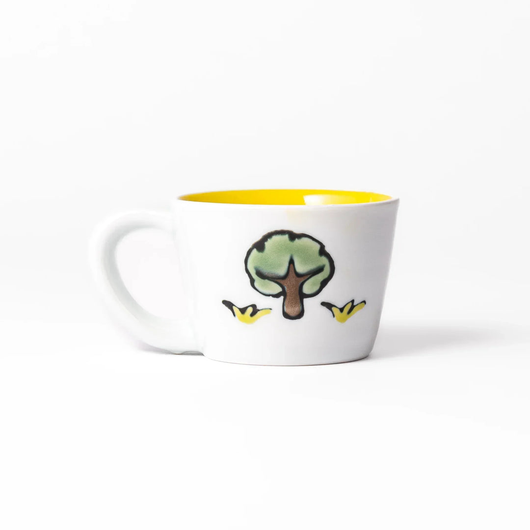 White ceramic kids’ mug with yellow giraffe and green ossicones, featuring a round handle and yellow interior.