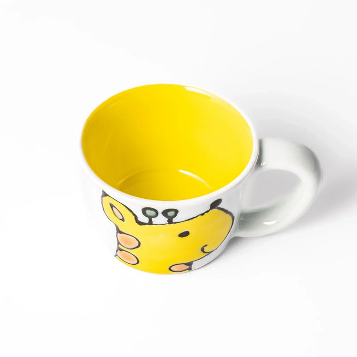 White ceramic kids’ mug with yellow giraffe and green ossicones, featuring a round handle and yellow interior.