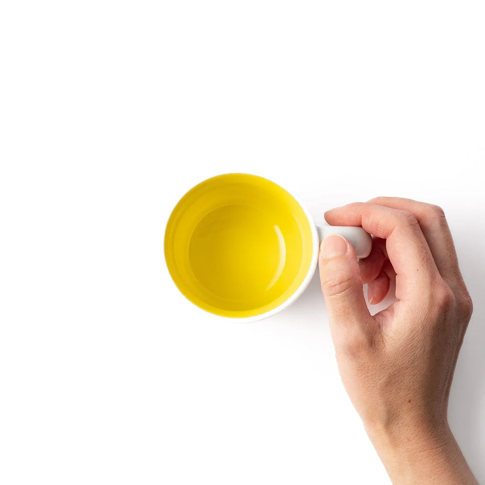 White ceramic kids’ mug with yellow giraffe and green ossicones, featuring a round handle and yellow interior.