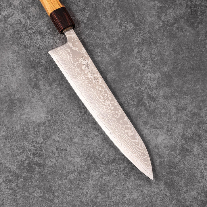 Japanese Damascus gyuto knife featuring a layered steel blade and natural wood handle displayed on gray stone background.