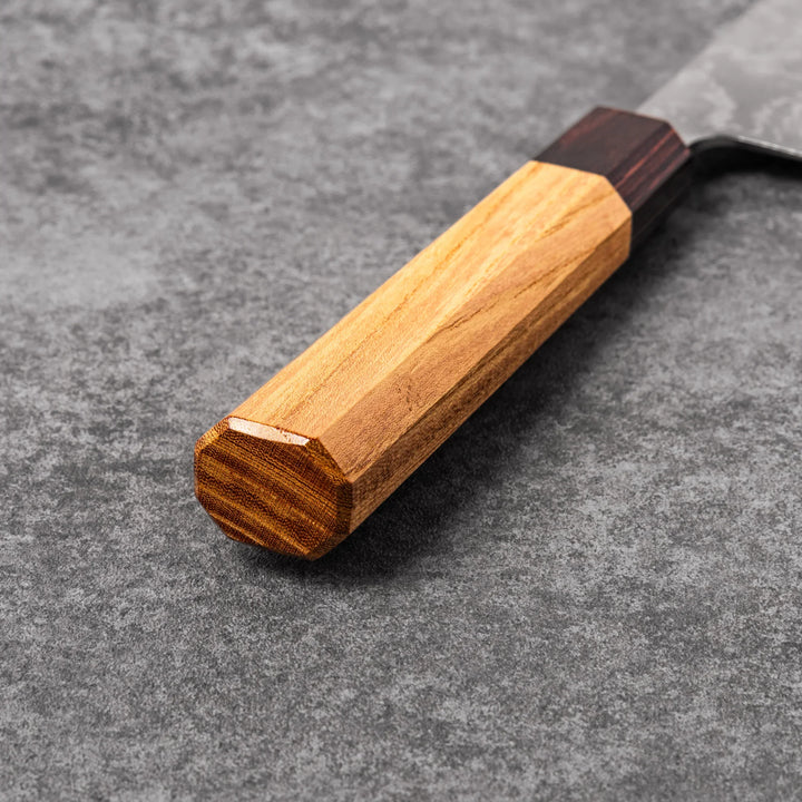 Japanese Damascus gyuto knife featuring a layered steel blade and natural wood handle displayed on gray stone background.