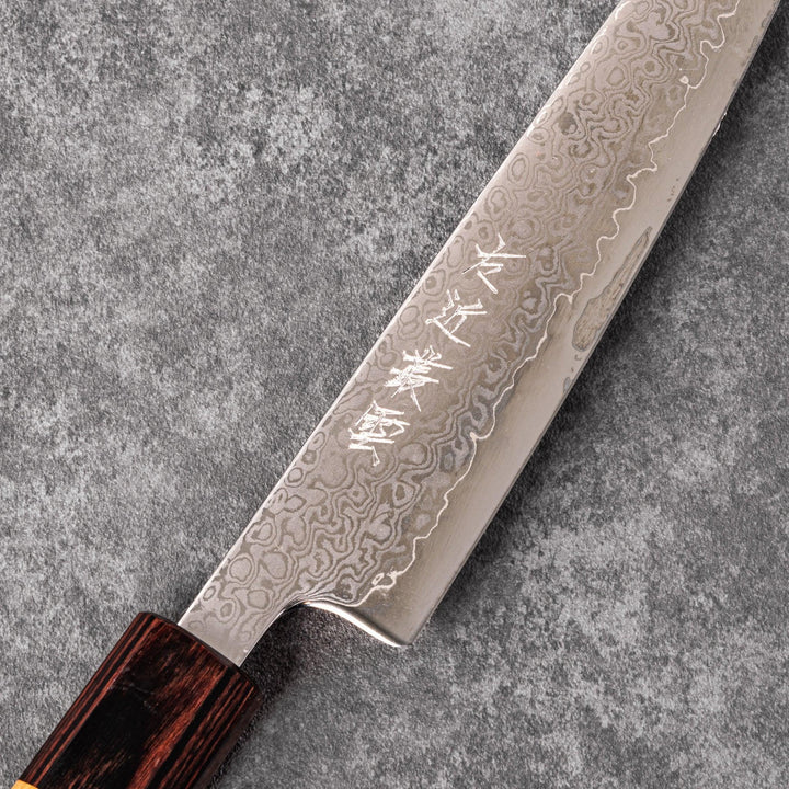Japanese Damascus petty knife with intricate layered steel blade and natural wood handle placed on gray stone surface.