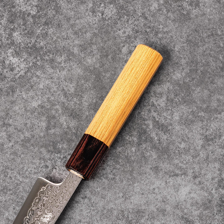 Japanese Damascus petty knife with intricate layered steel blade and natural wood handle placed on gray stone surface.